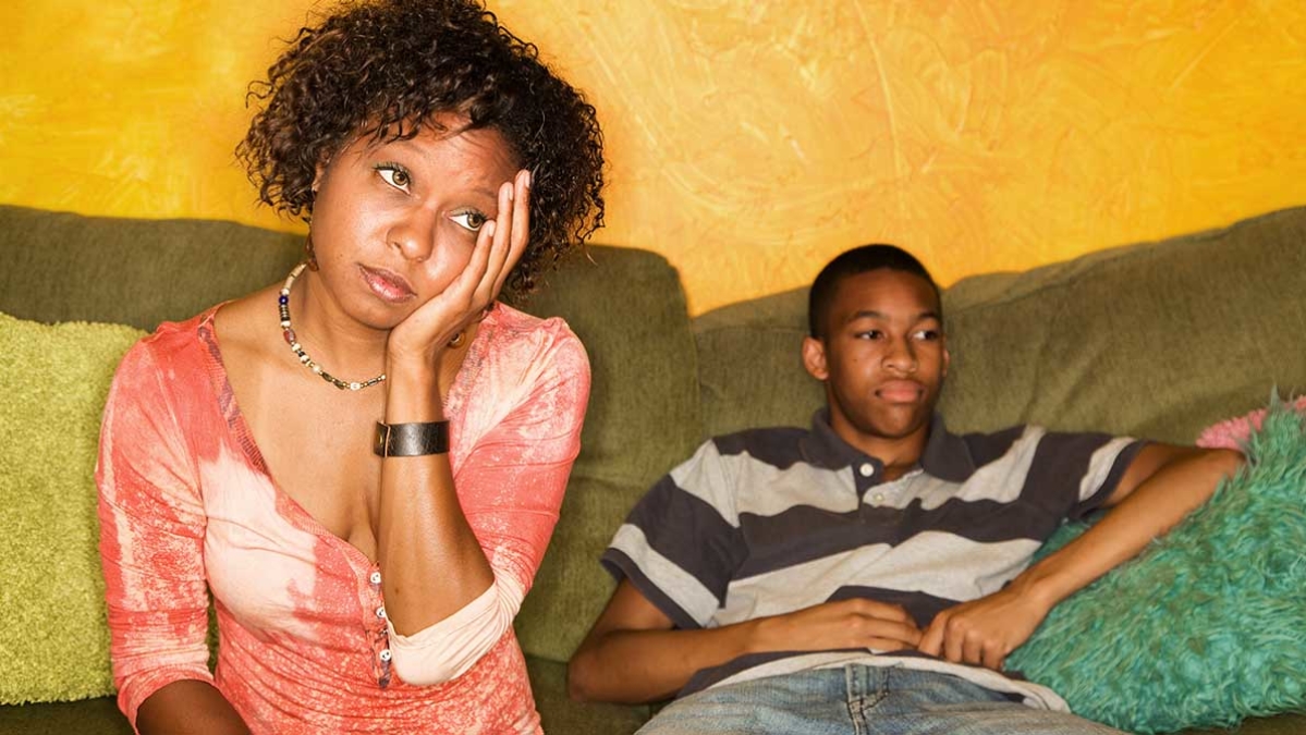 Mum and teenage son looking fed up in their lounge